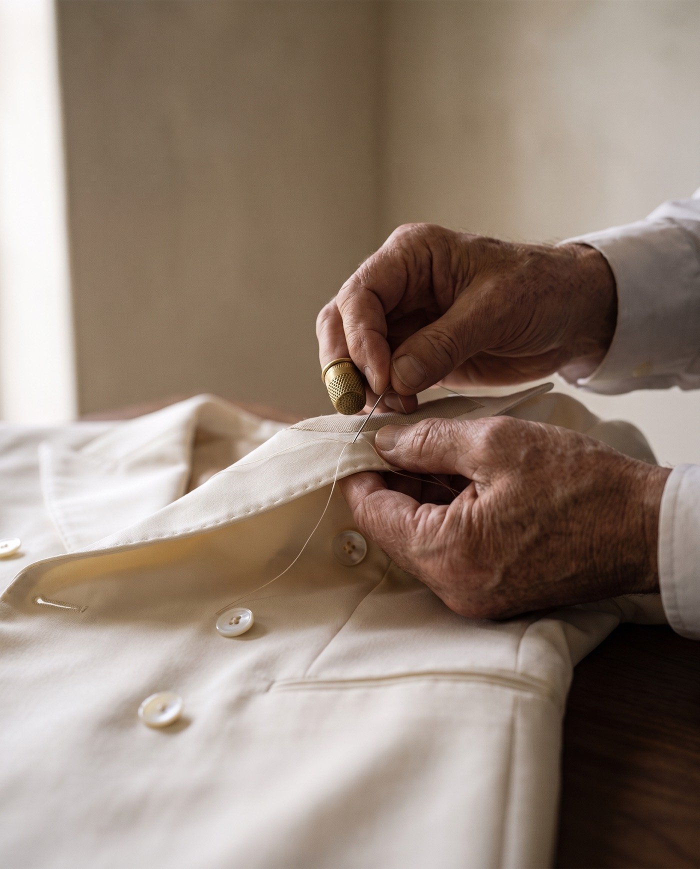 A master tailor's hands pad-stitch the ivory peak lapel with needle, thread and a brass thimble