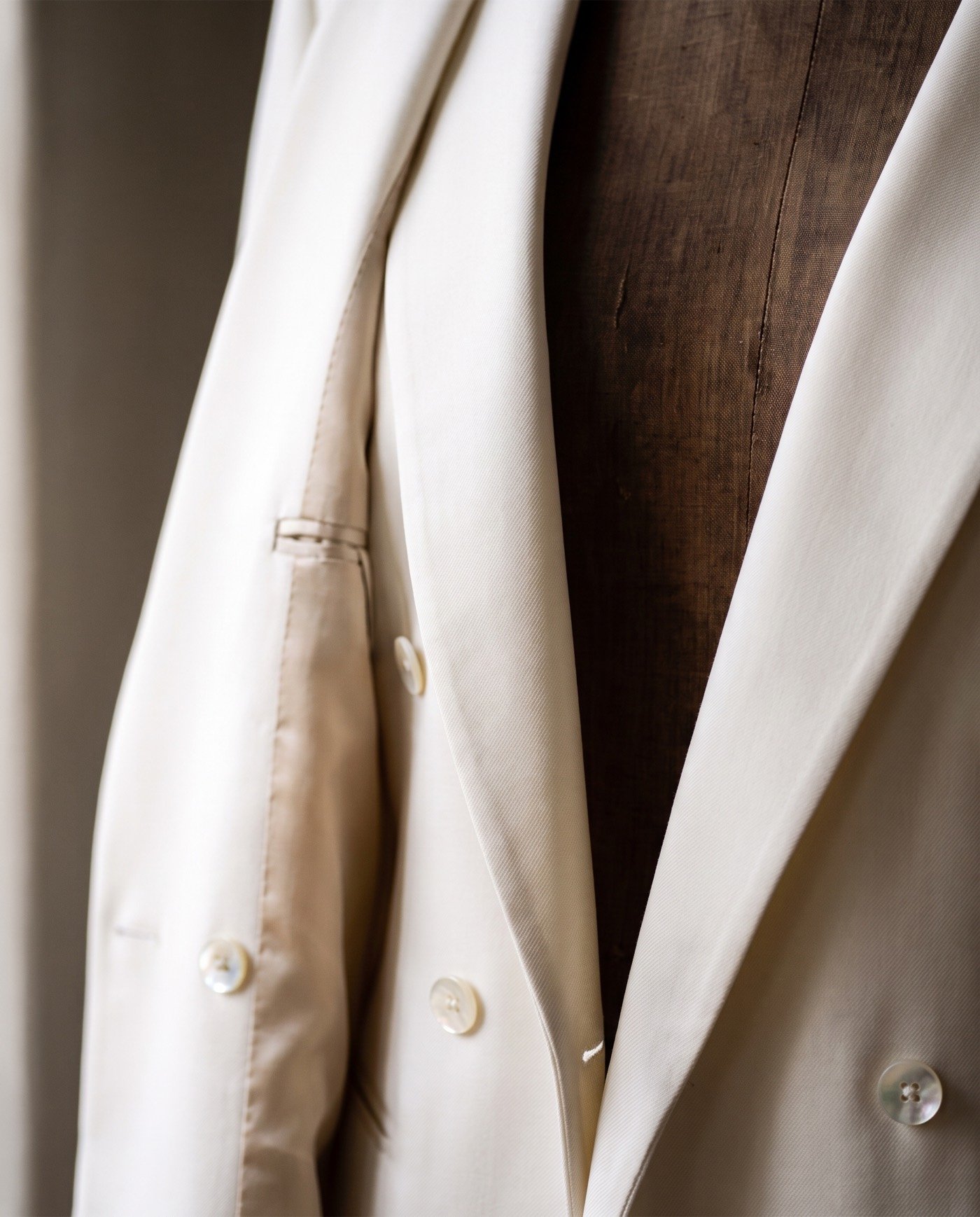 Close view of the Ligne Ivoire jacket on its walnut dress form: wide peak lapel, mother-of-pearl buttons and champagne silk lining in soft window light